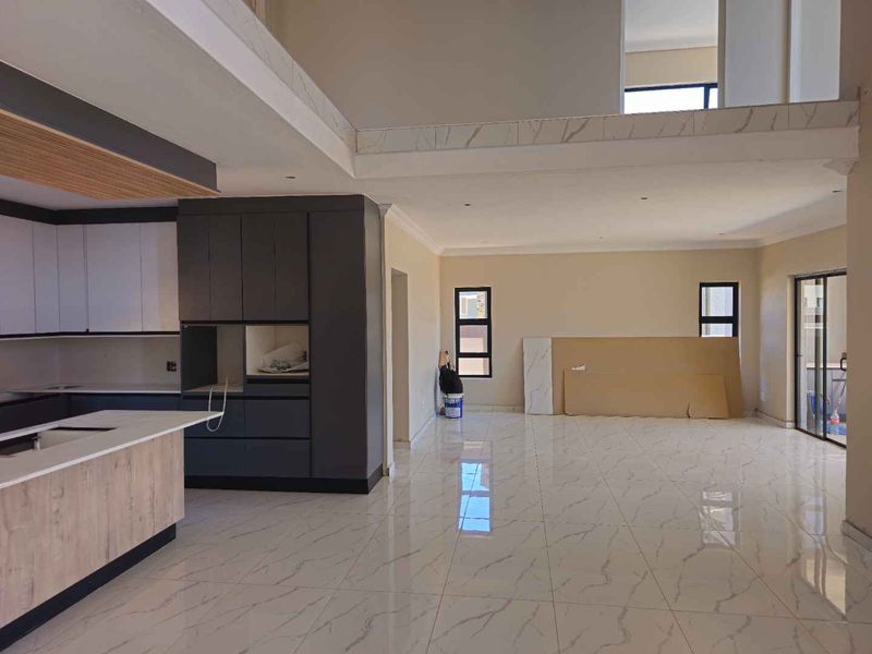 Spacious open-plan living area featuring modern kitchen cabinetry, a central island, and large porcelain floor tiles, currently in a near-complete state of construction.