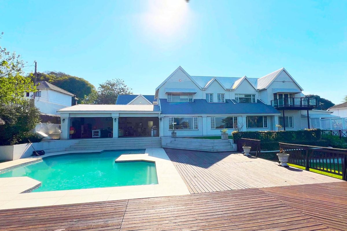 Spacious rear exterior featuring a large swimming pool, extensive timber decking, and a covered patio area overlooking the landscaped garden.