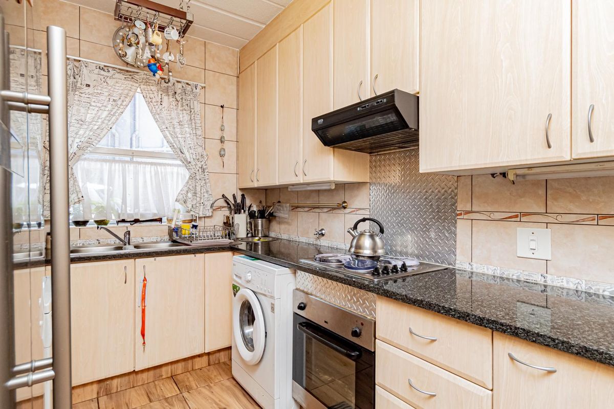 Functional kitchen featuring light wood cabinetry, granite countertops, built-in oven, gas hob, extractor fan, and integrated laundry appliance space.