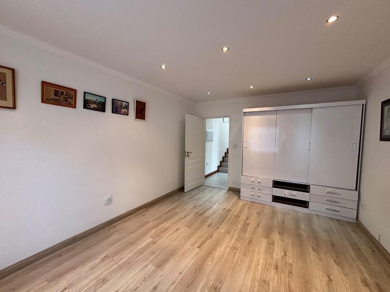 A well-maintained bedroom featuring light wood-look laminate flooring, recessed ceiling lighting, and a large white built-in wardrobe with integrated storage drawers.