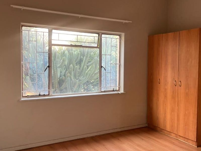 A bedroom featuring laminate flooring, a built-in wardrobe, and a window fitted with security bars.