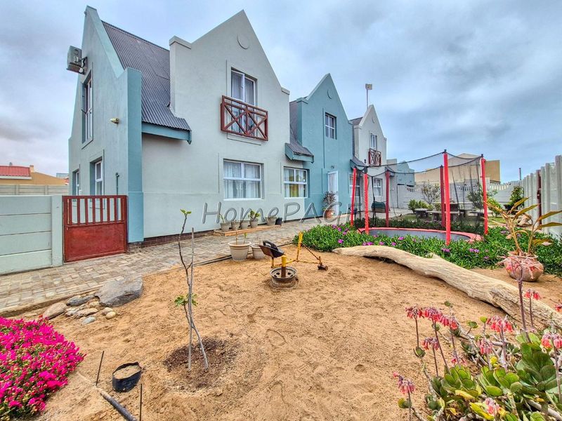 Rear view of a multi-story residential property featuring a paved patio area, landscaped garden, and secure boundary walling.