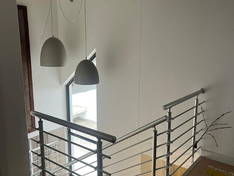 A bright, modern staircase landing featuring timber flooring, exposed rafters, and a sleek stainless steel balustrade with contemporary pendant lighting.