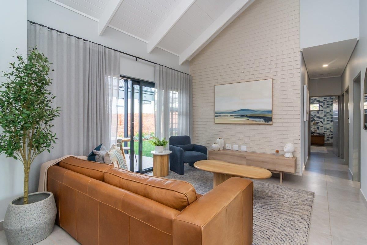 Bright living room featuring a vaulted ceiling with exposed beams, a painted brick feature wall, and large sliding glass doors leading to the garden.