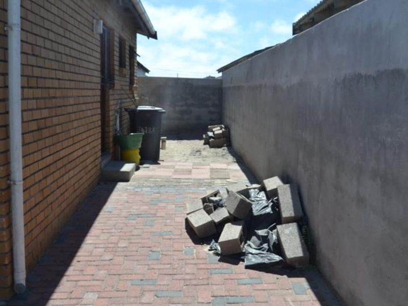 A narrow rear exterior side passage featuring brick paving and a boundary wall, currently requiring clearing of construction debris.