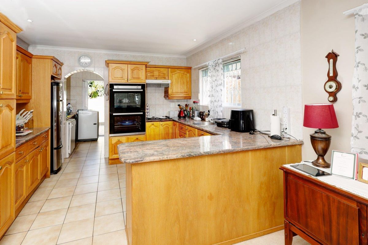 A functional kitchen featuring wooden cabinetry, granite countertops, a built-in double oven, and a tiled backsplash, with an adjacent scullery area.