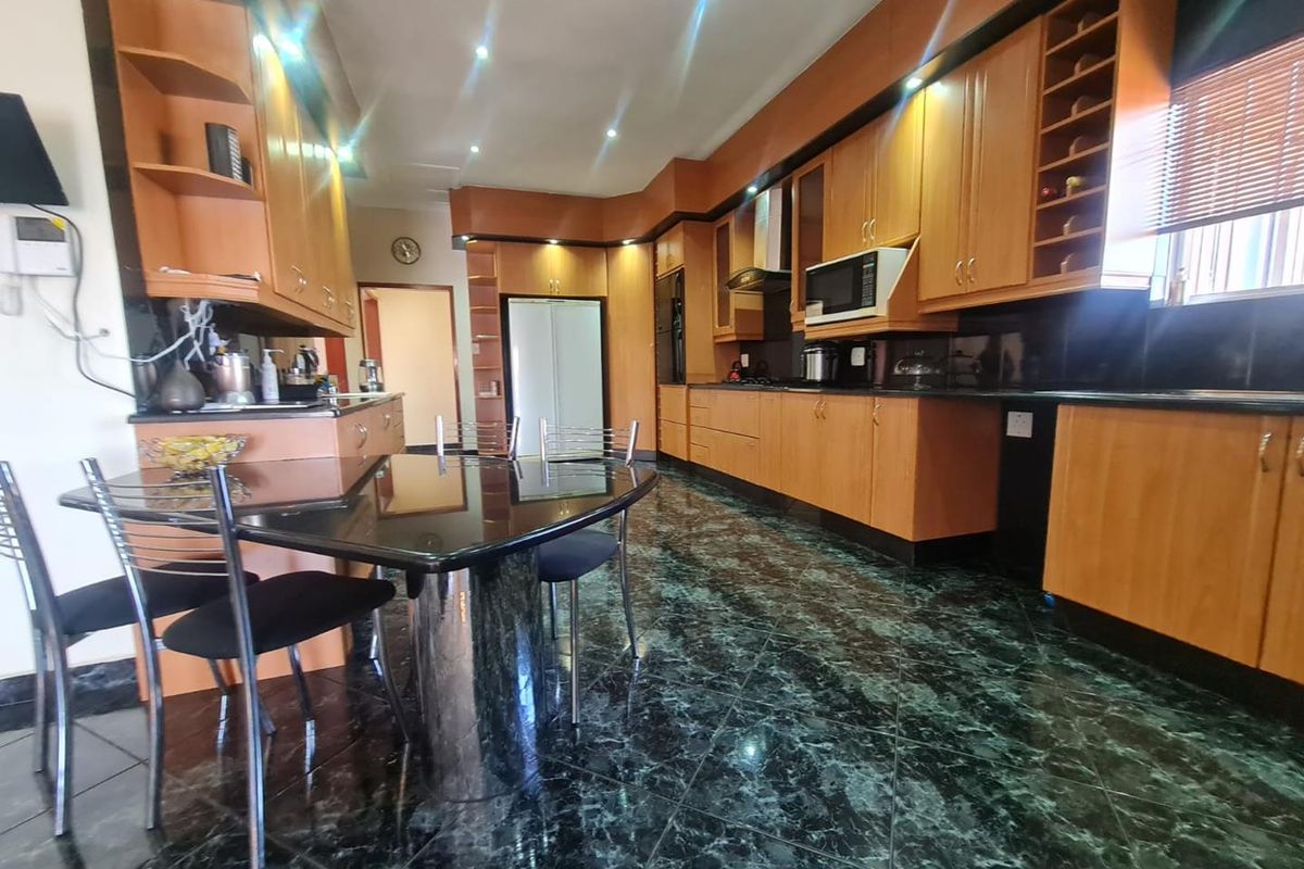 Spacious kitchen featuring extensive wooden cabinetry, dark granite countertops, integrated appliances, and polished green marble-effect floor tiles.