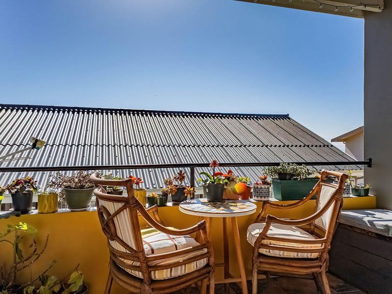 A sunny balcony featuring a metal railing, tiled flooring, and a built-in bench, offering an open outdoor space.