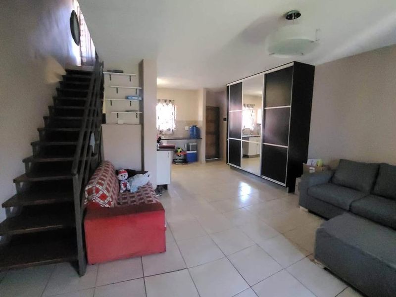 Open plan living area featuring tiled flooring, a staircase, and a large built-in wardrobe with mirrored doors.