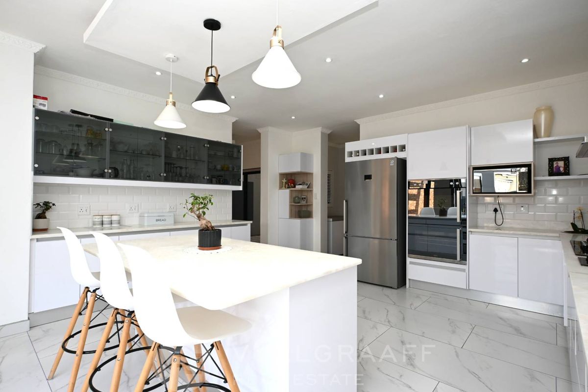Modern kitchen featuring a central island, sleek white cabinetry, subway tile backsplash, built-in appliances, and elegant marble-look flooring with contemporary pendant lighting.