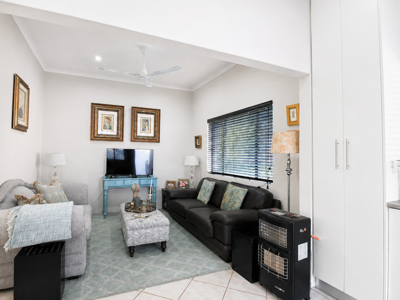 A bright and comfortable living room featuring tiled flooring, a ceiling fan, and built-in storage cupboards, offering a functional and well-maintained living space.