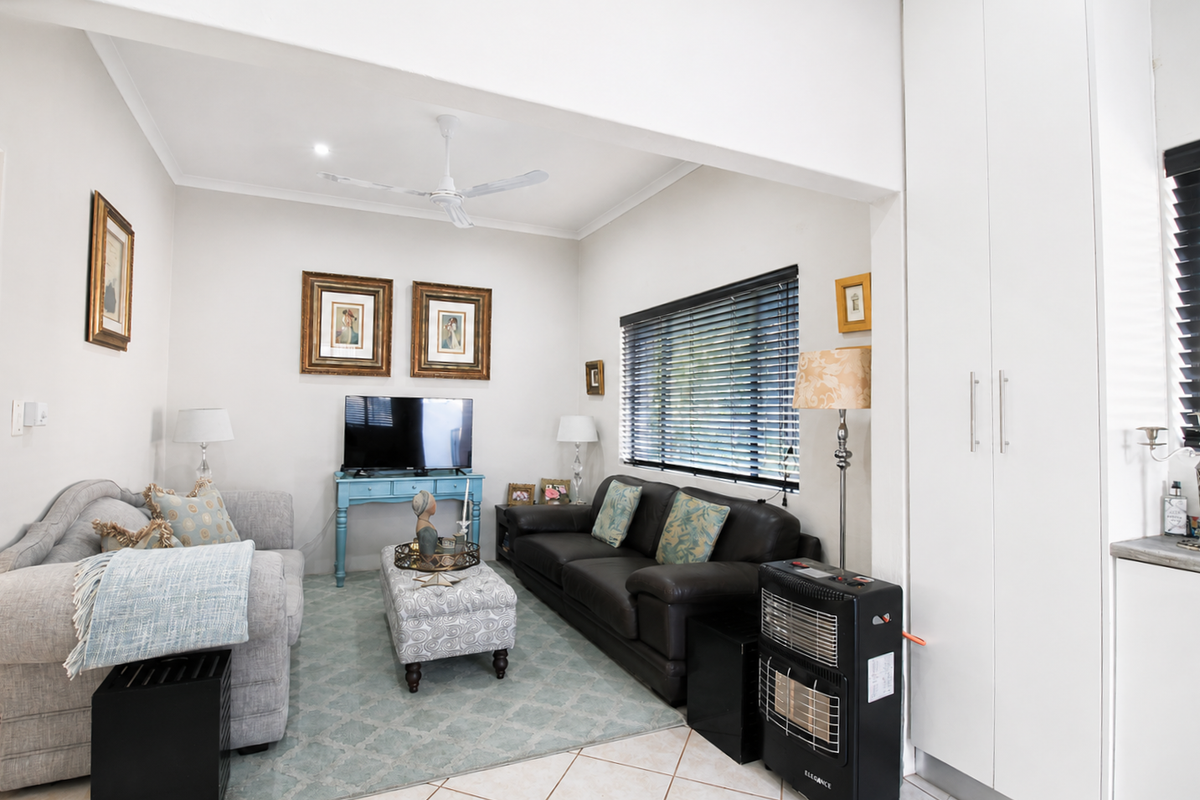A bright and comfortable living room featuring tiled flooring, a ceiling fan, and built-in storage cupboards, offering a functional and well-maintained living space.