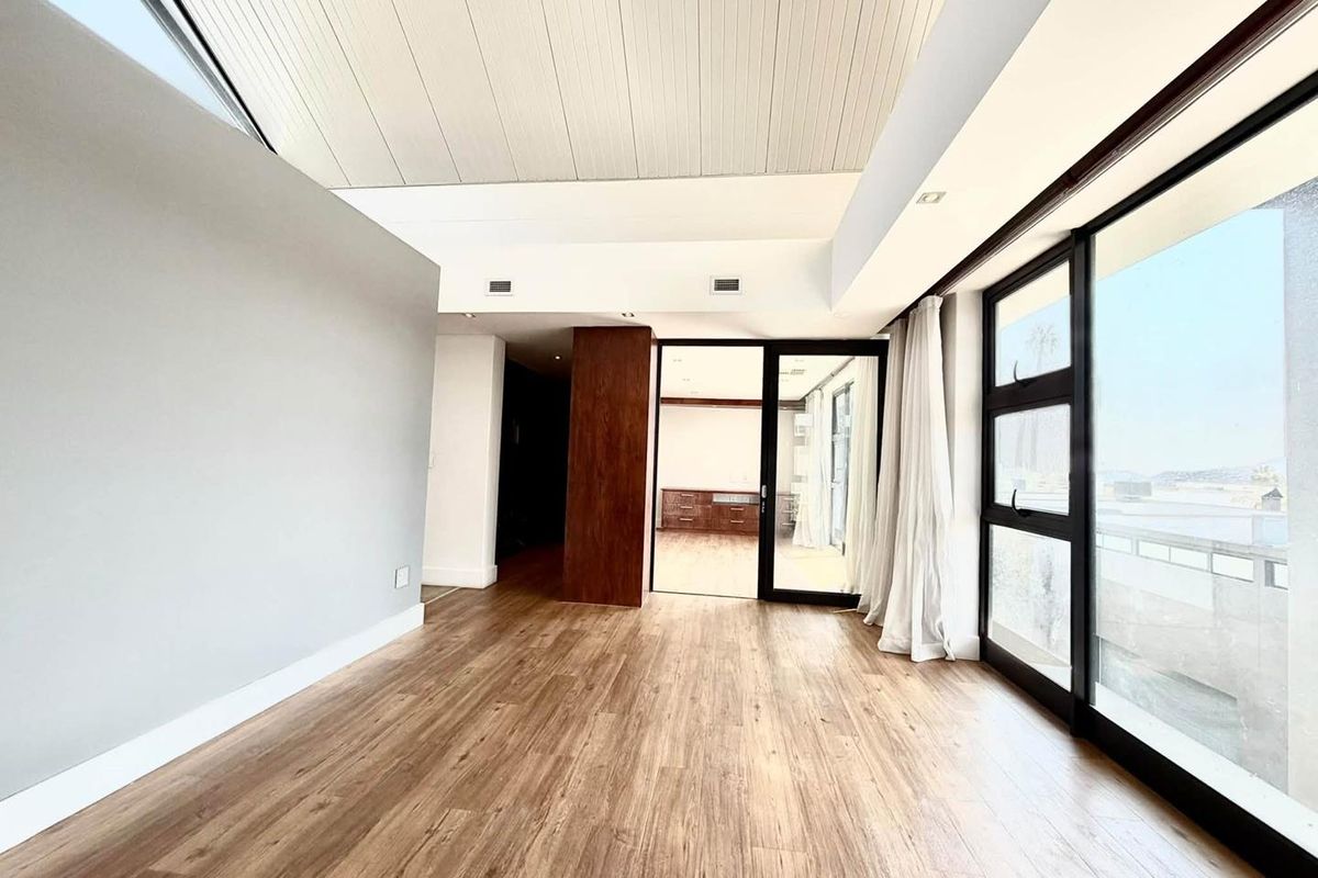 Spacious living area featuring timber flooring, a vaulted ceiling with a skylight, and large aluminium sliding doors leading to an outdoor space.