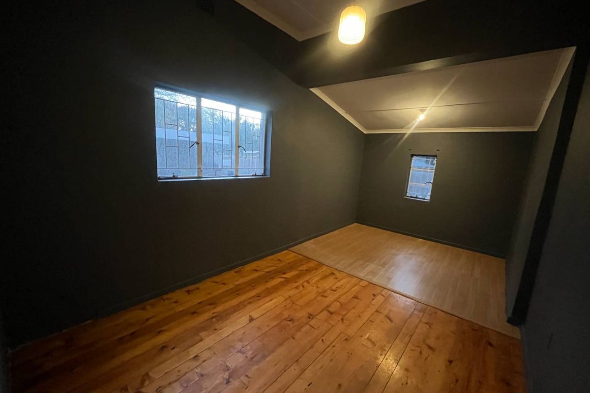 A spacious, empty room featuring dark painted walls, a combination of timber and laminate flooring, and security bars on the windows.