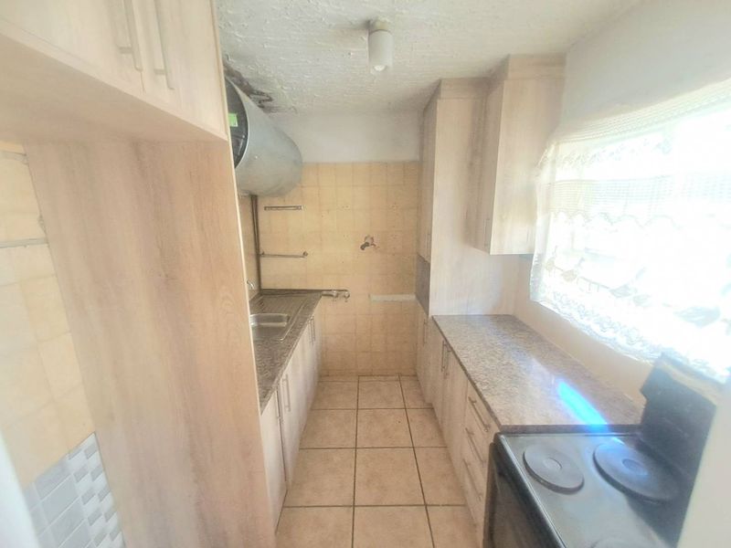A compact kitchen featuring laminate cabinetry, granite-look countertops, tiled flooring, and an exposed geyser, offering potential for modernization and improved layout efficiency.