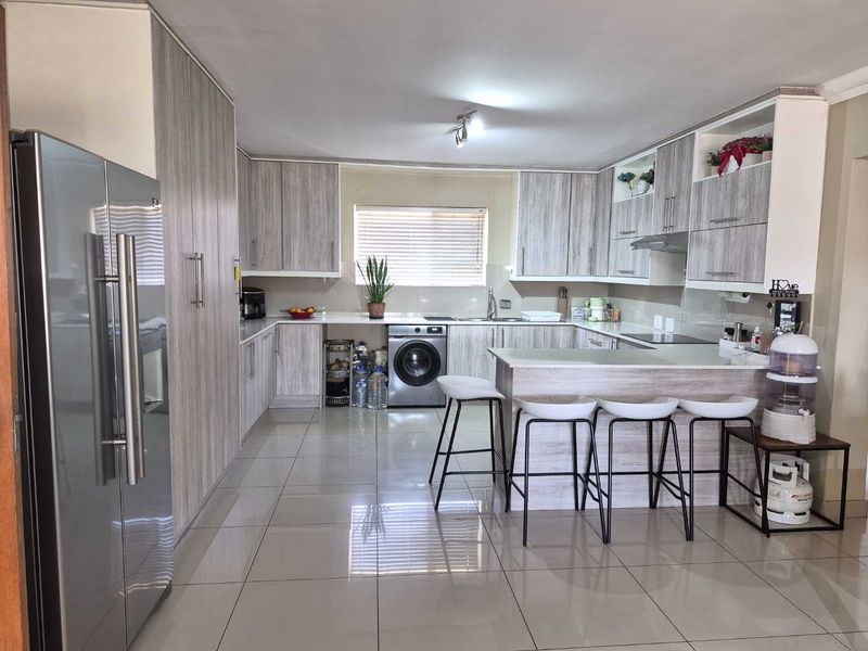 Modern kitchen featuring light wood-grain cabinetry, stone-look countertops, a breakfast bar, integrated washing machine, and sleek porcelain floor tiles.