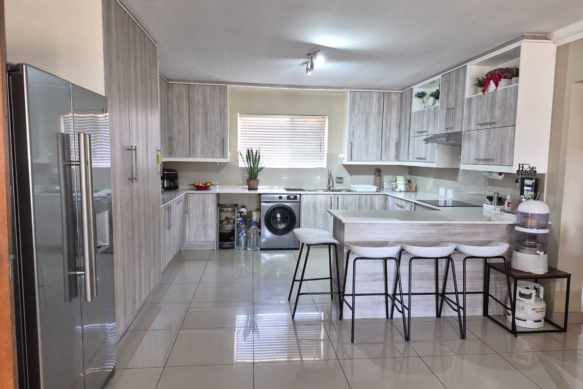 Modern kitchen featuring light wood-grain cabinetry, stone-look countertops, a breakfast bar, integrated washing machine, and sleek porcelain floor tiles.