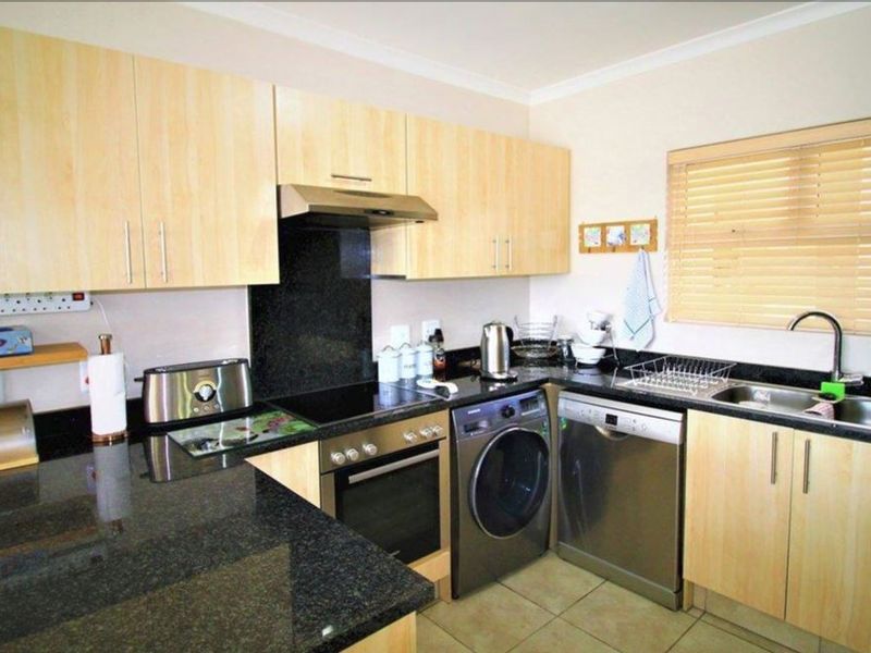 A functional kitchen featuring granite countertops, light wood cabinetry, built-in oven with extractor fan, and a double sink with tiled flooring.