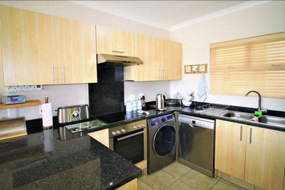 A functional kitchen featuring granite countertops, light wood cabinetry, built-in oven with extractor fan, and a double sink with tiled flooring.