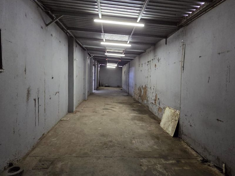 An empty, industrial-style utility space featuring concrete flooring, corrugated metal ceiling, and fluorescent lighting, requiring cosmetic refurbishment.