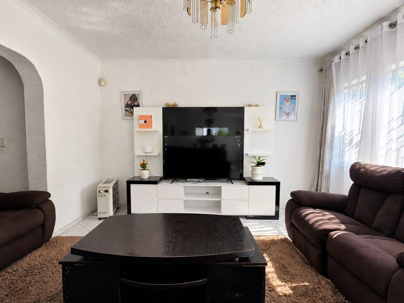 A comfortable living room featuring a built-in media unit, tiled flooring, and an arched entryway, providing a functional and well-lit space.