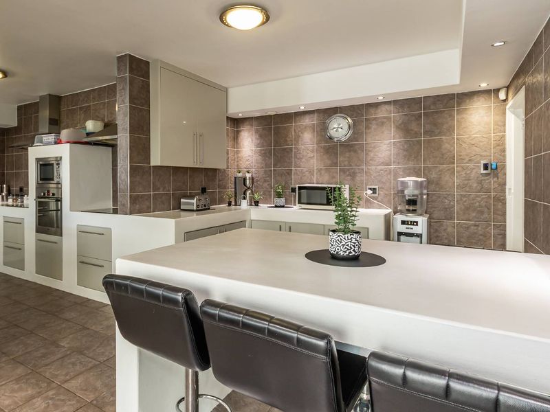 A functional kitchen featuring a central island, built-in oven, extractor fan, and tiled wall finishes with ample cabinetry for storage.