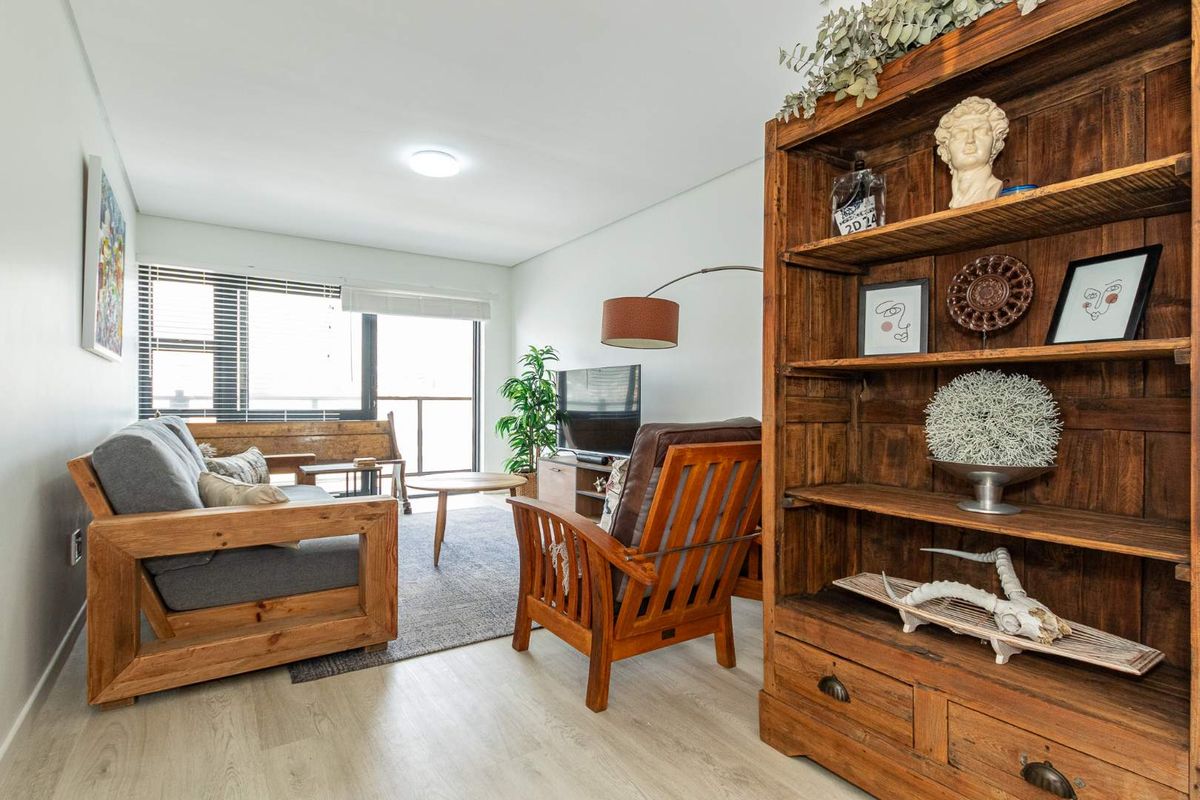 A bright and well-maintained living room featuring light wood-look flooring, large windows, and access to a balcony area.