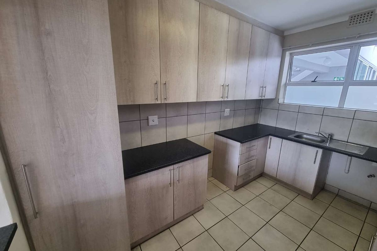 A clean and functional kitchen featuring light wood-tone cabinetry, dark granite countertops, tiled flooring, and a stainless steel sink.