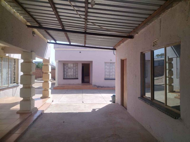 A covered outdoor patio area featuring concrete pillars, tiled flooring, and a corrugated metal roof, providing a functional transition space between building structures.