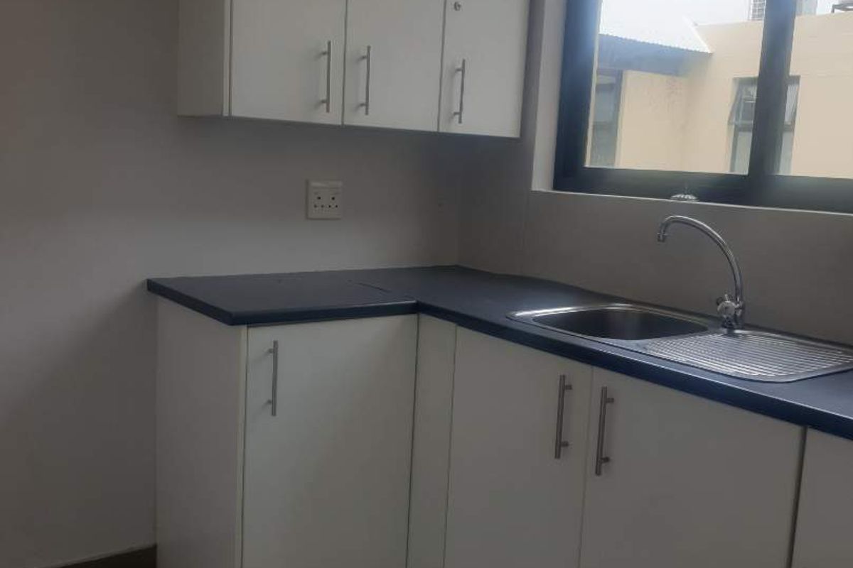A functional office kitchenette featuring white cabinetry, dark laminate countertops, and a stainless steel sink with a modern faucet.