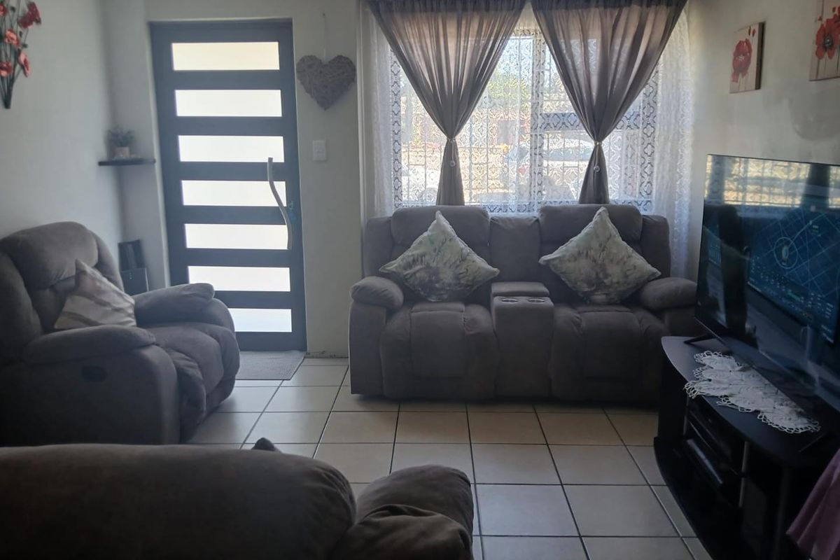 A cozy living room featuring tiled flooring, a modern front entrance door with horizontal glass panels, and a large window with security bars.