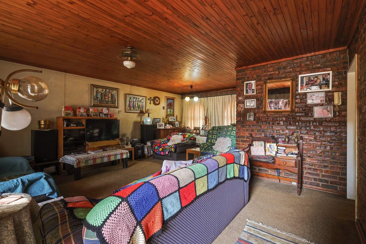 A living room featuring an exposed brick feature wall and a timber tongue and groove ceiling, offering a dated aesthetic with potential for modernization.
