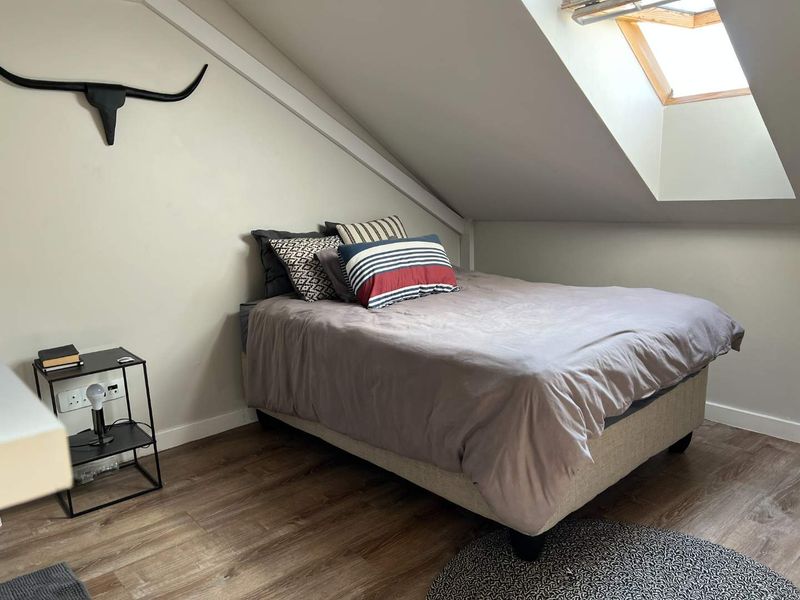 A cozy attic bedroom featuring a sloped ceiling, a skylight window for natural light, and durable laminate flooring.