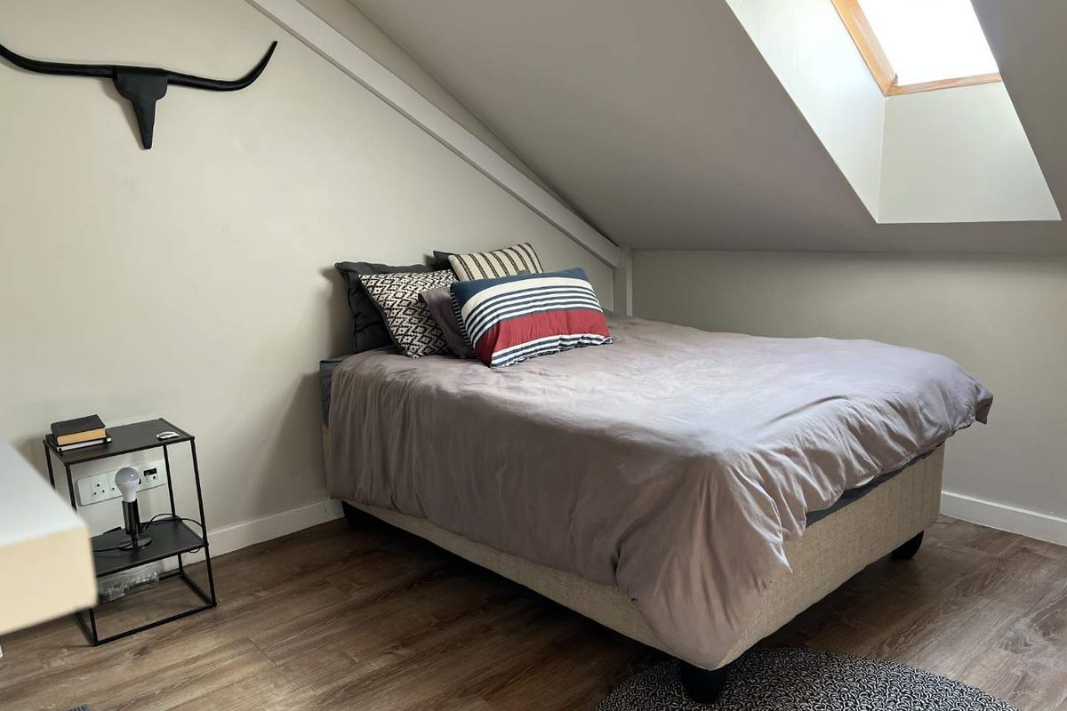 A cozy attic bedroom featuring a sloped ceiling, a skylight window for natural light, and durable laminate flooring.