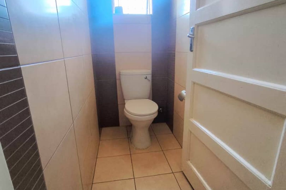 A compact, tiled guest bathroom featuring a standard toilet and a small window for natural light.