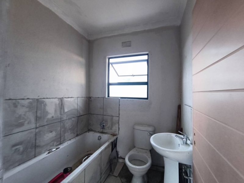 A bathroom in need of renovation, featuring a bathtub, toilet, and pedestal basin with unfinished wall surfaces and incomplete tiling.