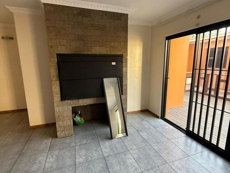 Spacious living area featuring a built-in fireplace with stone cladding, large sliding glass doors leading to an outdoor space, and neutral tiled flooring.