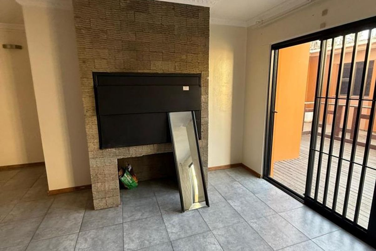 Spacious living area featuring a built-in fireplace with stone cladding, large sliding glass doors leading to an outdoor space, and neutral tiled flooring.