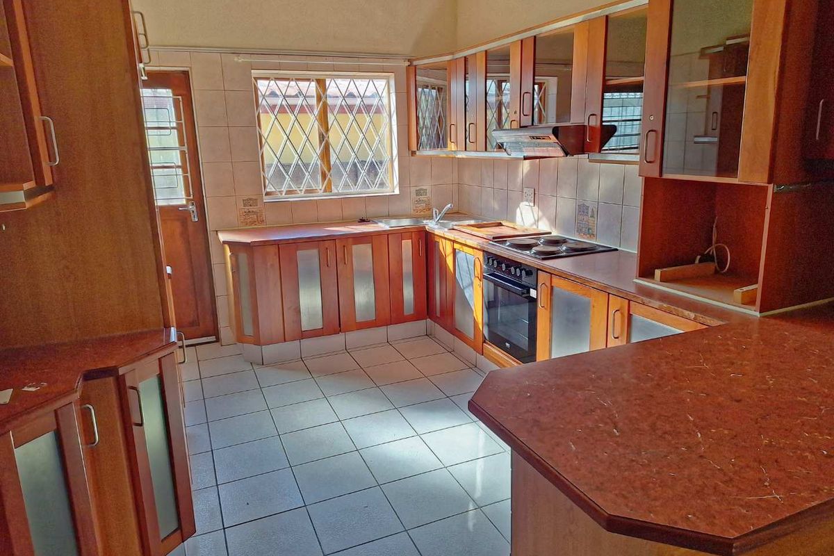 A functional kitchen featuring wooden cabinetry, built-in oven and hob, tiled flooring, and security bars on the window and door.