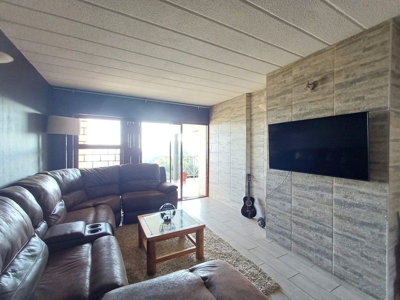A living room featuring tiled flooring, a stone-clad feature wall, and a sliding glass door providing access to an outdoor area.