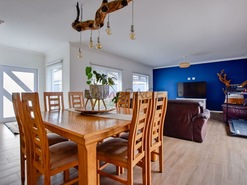 An open-plan living and dining area featuring tiled flooring, a bold blue feature wall, and modern lighting fixtures.