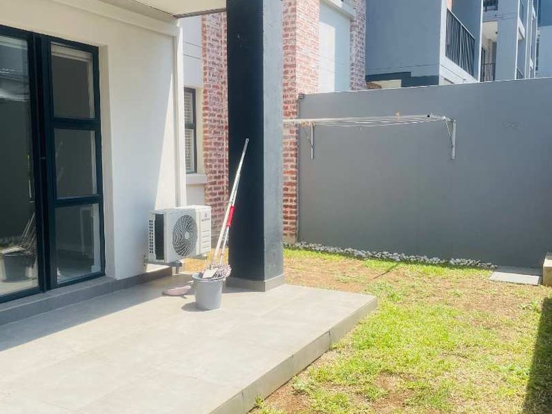 A private ground-floor patio area featuring tiled flooring, a small lawn, and a wall-mounted clothesline, accessible via sliding glass doors.