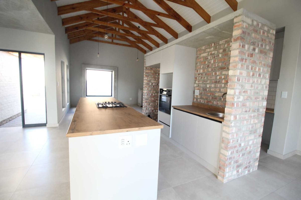 Modern kitchen featuring exposed timber trusses, a central island with gas hob, and industrial-style exposed brick accents with concrete and wood finishes.