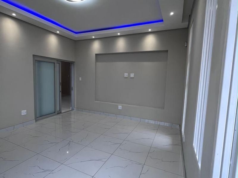 Modern, empty living area featuring high-gloss marble-look floor tiles, recessed ceiling lighting with blue LED accents, and a built-in wall niche.