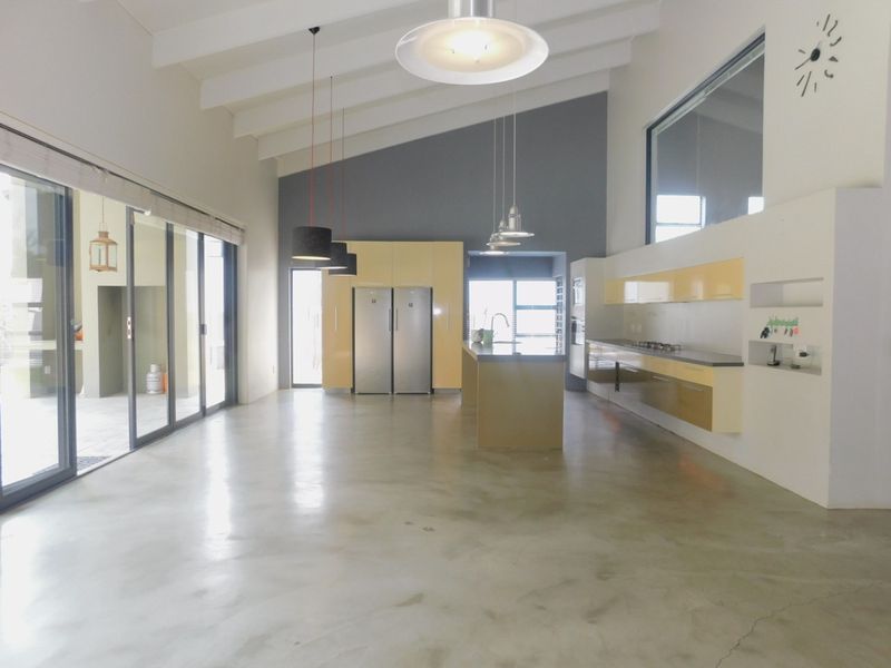Spacious open-plan kitchen and living area featuring polished concrete floors, vaulted ceilings, modern cabinetry, and large sliding doors leading to the patio.