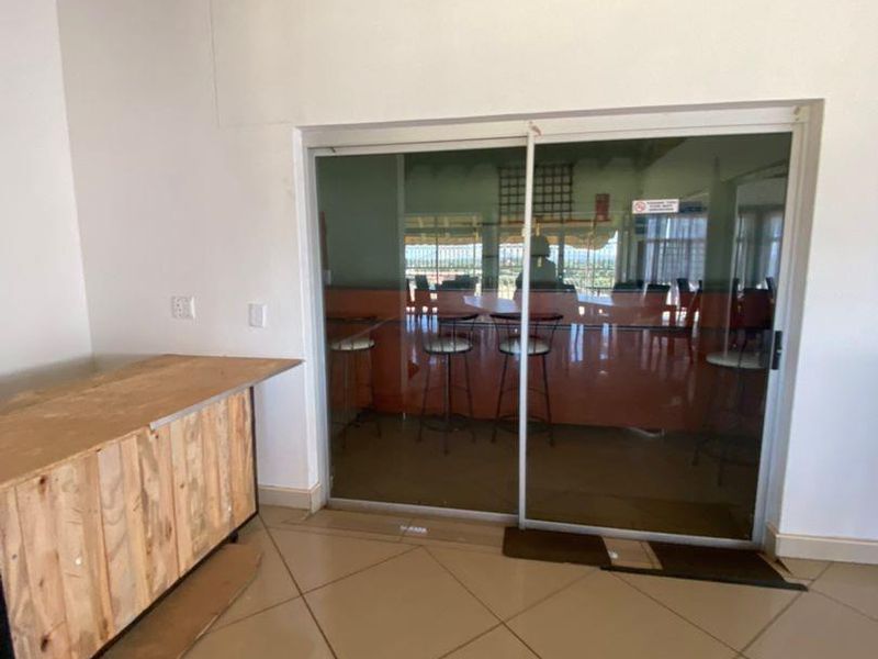 An interior space featuring tiled flooring and a large sliding glass door leading to an outdoor area, currently containing an unfinished wooden counter unit.