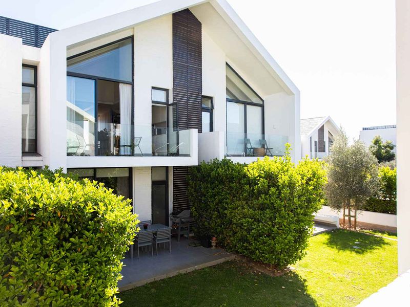 Rear view of a modern apartment building featuring a covered patio, glass balustrades, and a well-maintained private garden area.