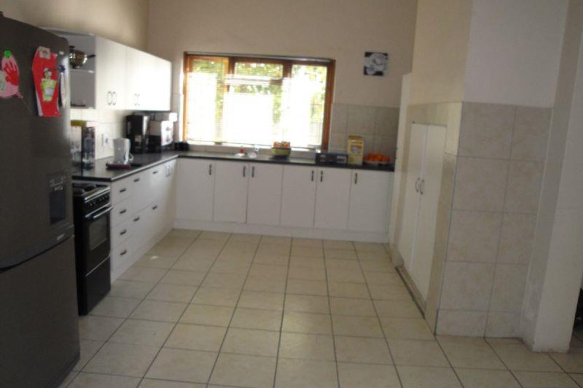 Functional kitchen featuring white cabinetry, tiled flooring, tiled splashbacks, and a double sink with a window overlooking the exterior.