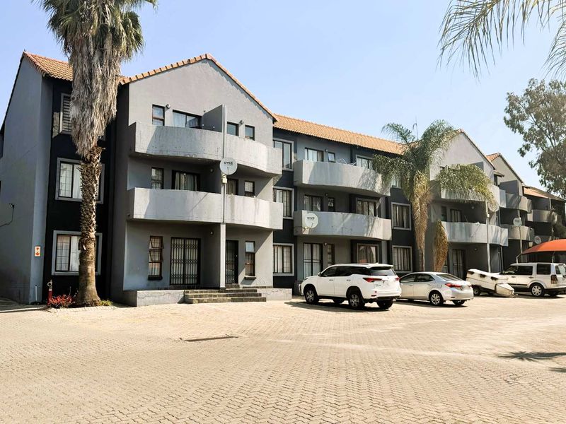 Exterior view of a multi-story apartment complex featuring paved parking, private balconies, and a tiled roof structure.