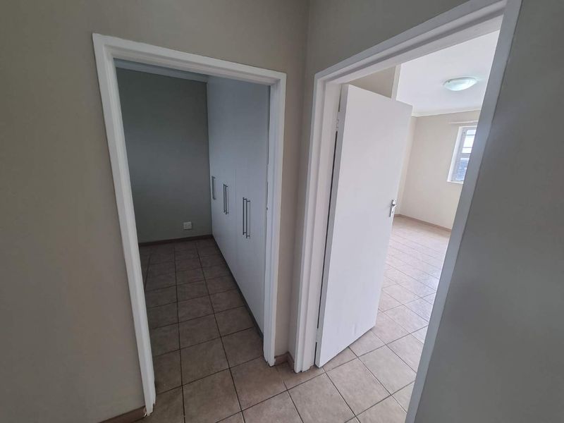 A clean hallway featuring tiled flooring and access to a bedroom with built-in cupboards.